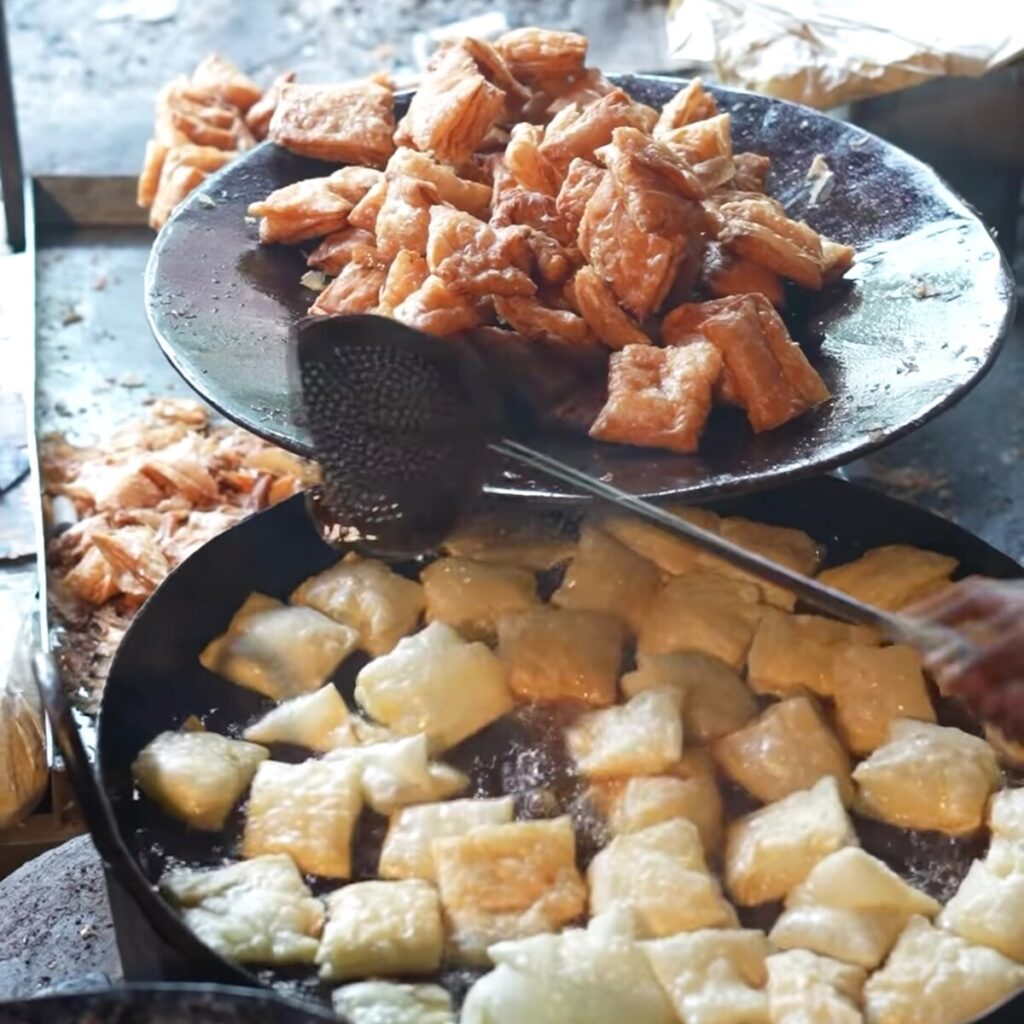 Master halwai scooping fresh-fried khaja from iron kadhai with a brass ladle in Silao, Bihar