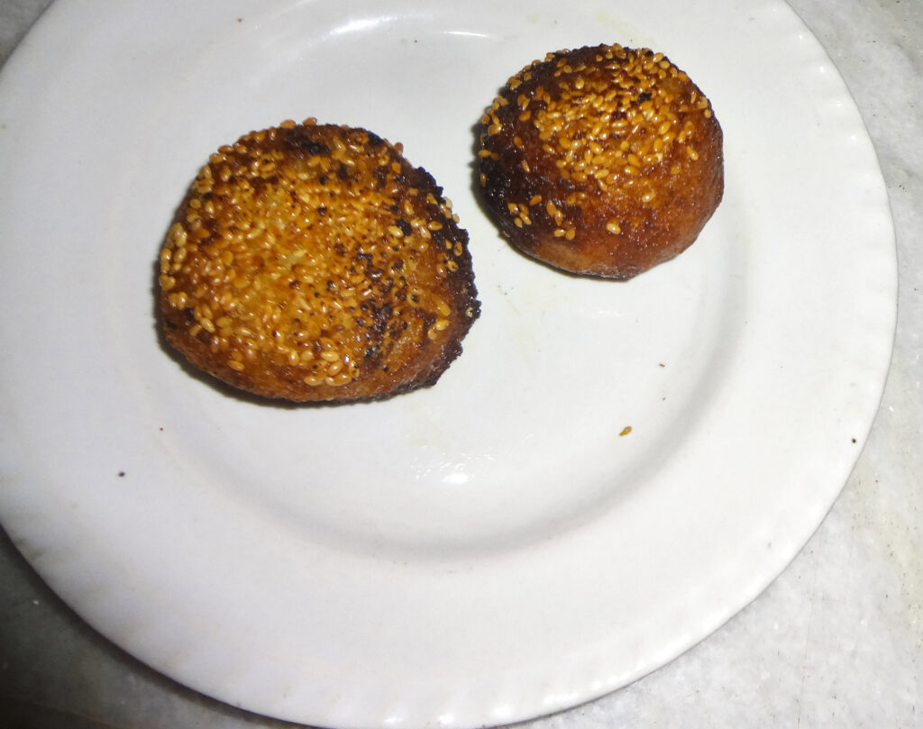 Bihari Anarsa rice-flour and sesame sweet — two golden sesame-crusted discs on a plate