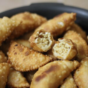 Golden deep-fried Mithila pedakiya in a bowl, two split open to reveal the pale khoya and coconut filling inside