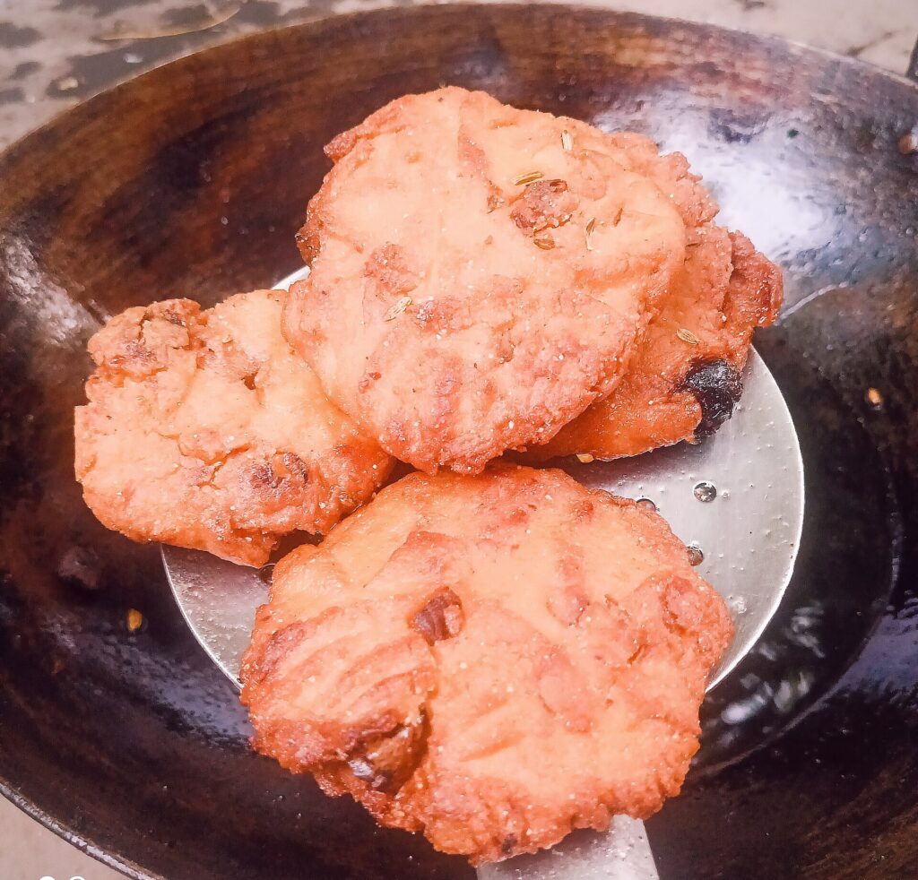 Freshly ghee-fried Thekua speckled with fennel seeds on a dark plate — crisp wheat and jaggery sweet from Bihar