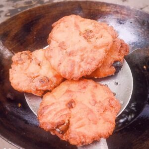Freshly ghee-fried Thekua speckled with fennel seeds on a dark plate — crisp wheat and jaggery sweet from Bihar