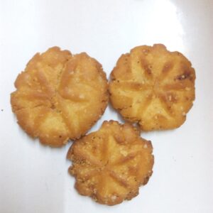 Three golden Thekua cookies on a white plate showing the traditional floral mould pattern — pure ghee Bihari Chhath sweet