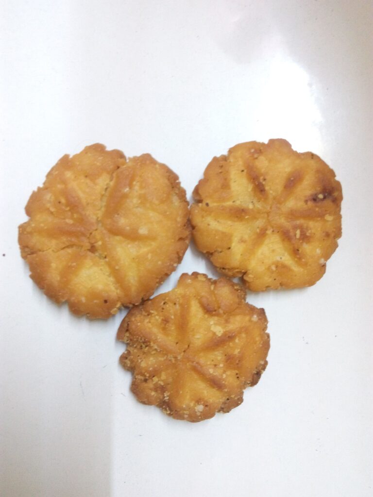Three golden Thekua cookies on a white plate showing the traditional floral mould pattern — pure ghee Bihari Chhath sweet